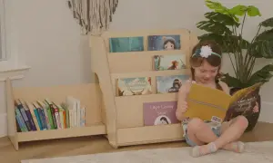 A young girl reads a book next to a DIY Montessori bookshelf filled with children's books.