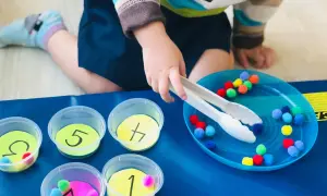 Toddler sorting colorful pom-poms into numbered cups. A fun activity for what to do with toddlers at home, practicing fine motor skills and number recognition.