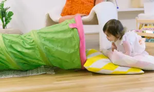 A toddler explores a green play tunnel, engaging in fun climbing activities. Colorful pillows add to the playful scene.