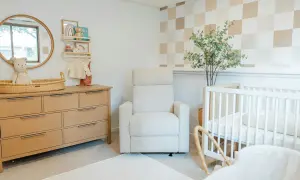Cozy and modern nursery with a wooden dresser, plush recliner, and crib. This room offers sweet, cute baby room ideas with its neutral palette and playful checkered wallpaper.