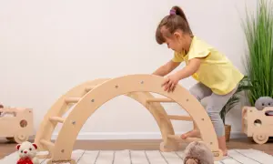 A young girl in a yellow shirt climbs a wooden arch, showcasing gross motor activities.