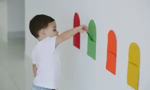 A toddler explores bright colors for 1 year old, placing a green paper strip into a matching pocket on a white wall.
