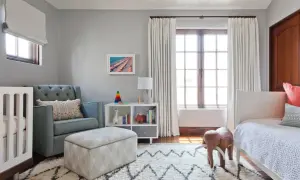 A cozy nursery features a tufted blue couch, a crib, and a white bookshelf filled with toys and books.