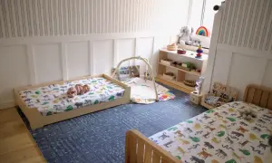 A baby sleeps on a low bed with animal print sheets, embodying the Montessori sleep on floor philosophy. Toys and a play mat are nearby.