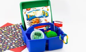 A blue caddy holds items for a sensory box: TheraPutty, a liquid timer, a spiky ball, and building blocks.
