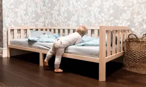 A toddler climbs into a Montessori bed, showcasing its low profile and ideal dimensions for independent exploration.