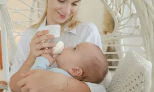 A mother smiles lovingly while holding her baby for upright bottle feeding. The baby is nestled in her arms, taking milk from the bottle.