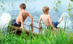 Two boys enjoy parallel play, splashing water from a wooden dock.