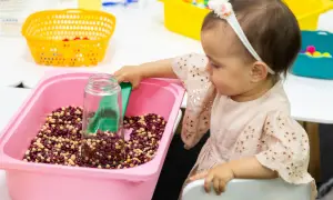 A baby girl explores a winter sensory bin filled with beans and a scoop.