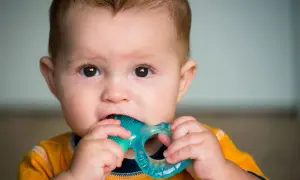 Baby chews on a blue teething ring, seeking relief. Does pacifier help with teething? This little one is finding comfort in a chew toy.