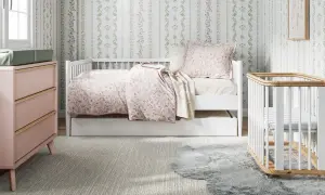 A charming small nursery features a white daybed with floral bedding, a pink dresser, and a white crib.