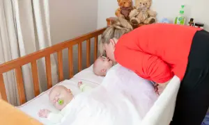 A mother kisses her baby in one of two **double baby cribs**. Another baby sleeps peacefully nearby.