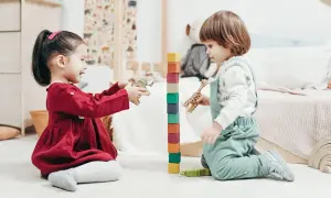 Two toddlers engage in fun games to play with one year old, stacking colorful blocks and playing with wooden animals.