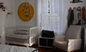 Cozy nursery nook ideas: a white crib, a comfy armchair, and a wall decorated with a sun mural and a New York pennant.