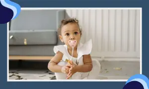 A baby girl with a pink pacifier in her mouth sits on the floor, her eyes wide with curiosity. The pacifier terth is a comforting presence as she explores her surroundings.