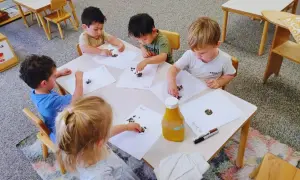 Children engage in child led learning, placing seeds on paper at a table.