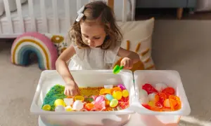 A young girl explores colorful rice and toys in sensory bins, demonstrating why sensory bins are important for early childhood development and learning through play.