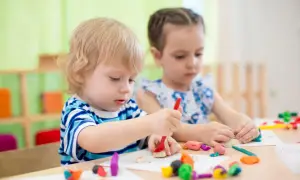 Two children engage in parallel play vs associative play, molding colorful clay at a table.