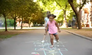 Kids learn shapes like squares and rectangles when playing hopscotch. Two girls are playing hopscotch on a sunny day.