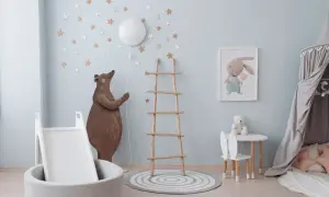 A whimsical nursery room, perfect for learning how to paint a nursery room. A bear holds a balloon, stars adorn the walls, and a bunny picture hangs above a small table.