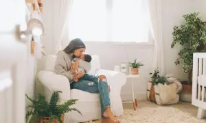 A mother cradles her baby in a cozy nursery, surrounded by soft decor and plants, hinting at peaceful nursery themes.
