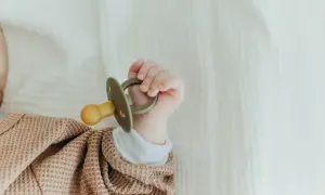 A tiny hand holds a pacifier that appears too big for a newborn, nestled in a soft, textured blanket.
