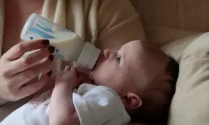 A baby drinks from a bottle. Concerns exist about does bottle feeding affect teeth alignment, but this image focuses on a moment of nourishment.
