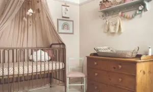 Dreamy small nursery ideas for a girl, featuring a gold crib with a cloud pillow, a rainbow print, and a vintage dresser.