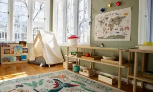 A bright, airy room with a cozy montessori home setup. A tent, world map, and wooden shelves filled with books and toys create a playful learning environment.