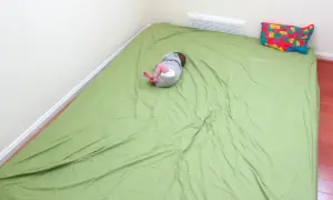 A baby sleeps on a green mattress on the floor, a simple setup for how to make a floor bed for baby. A colorful map pillow rests nearby.