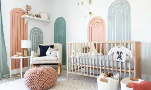A modern nursery with rainbow wall art, a crib, and a comfy chair. Perfect for twin nursery themes with its neutral colors and playful design.