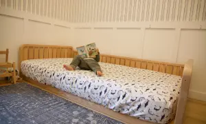 A child reads a book on a DIY Montessori bed with shark-patterned sheets.