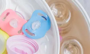 Pink and blue pacifiers sit in a sterilizer with baby bottles. Learn how to sterilize pacifier safely for your baby.