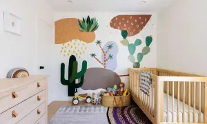 A colorful gender neutral nursery with a desert mural, wooden crib, dresser, and toys.