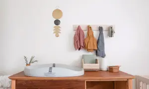 Chic corner nursery ideas: A changing pad sits on a wooden dresser with baby clothes hanging on a wall rack.