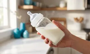 Hand holding a baby bottle filled with milk. The nipple appears to be a fast flow, indicating signs nipple flow is too fast.
