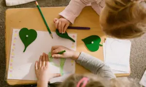 Children engage in Montessori fine motor activities, drawing and manipulating leaf shapes on a wooden table.