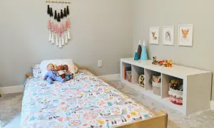 A cozy floor bed setup with a woodland-themed duvet cover, dolls, and a wall hanging. A white cube shelf holds books and toys.