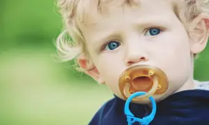 A toddler with blue eyes and blonde hair has a pacifier in their mouth. This image prompts the question: can pacifiers cause cavities?