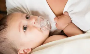 A baby with a pacifier, nestled close to their mother's chest, perhaps after breastfeeding.