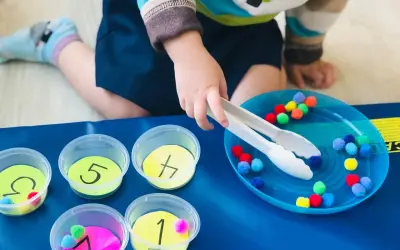 Toddler sorting colorful pom-poms into numbered cups. A fun activity for what to do with toddlers at home, practicing fine motor skills and number recognition.