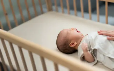 A baby yawns in a wooden crib. This image reassures parents that mini cribs are safe for their little ones.