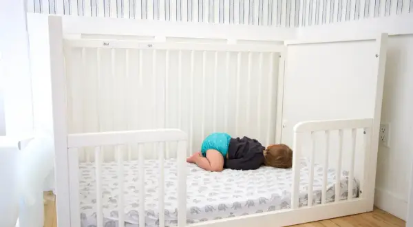 A baby sleeps on a floor bed with an elephant print sheet. This setup raises questions about whether floor beds are safe for babies.