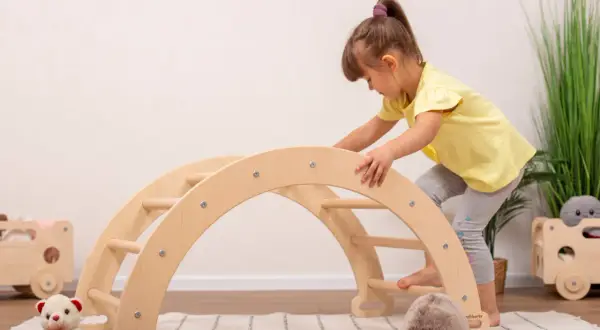 A young girl in a yellow shirt climbs a wooden arch, showcasing gross motor activities.