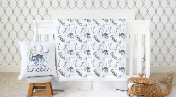 Nautical nursery with under the sea crib bedding sets featuring octopuses, narwhals, and jellyfish. A whale basket sits nearby.