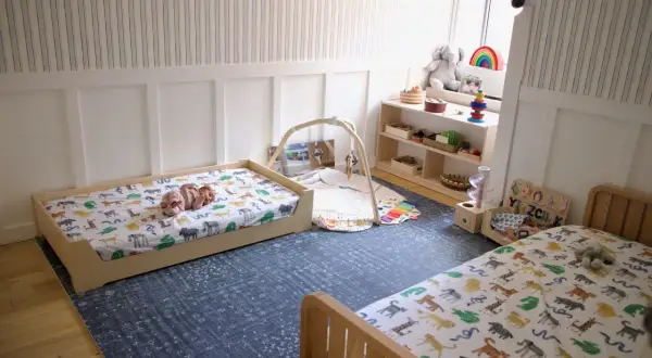 A baby sleeps on a low bed with animal print sheets, embodying the Montessori sleep on floor philosophy. Toys and a play mat are nearby.