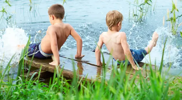 Two boys enjoy parallel play, splashing water from a wooden dock.