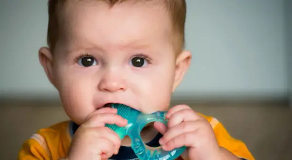 Baby chews on a blue teething ring, seeking relief. Does pacifier help with teething? This little one is finding comfort in a chew toy.