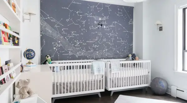 Two white cribs in a nursery with a constellation mural. This is a perfect example of baby boys nursery designs, inspiring dreams of the stars.