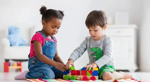 Two children engage in parallel play, building a colorful wooden train with blocks.